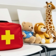 First aid bag and stuffed animals on white chairs indoors.